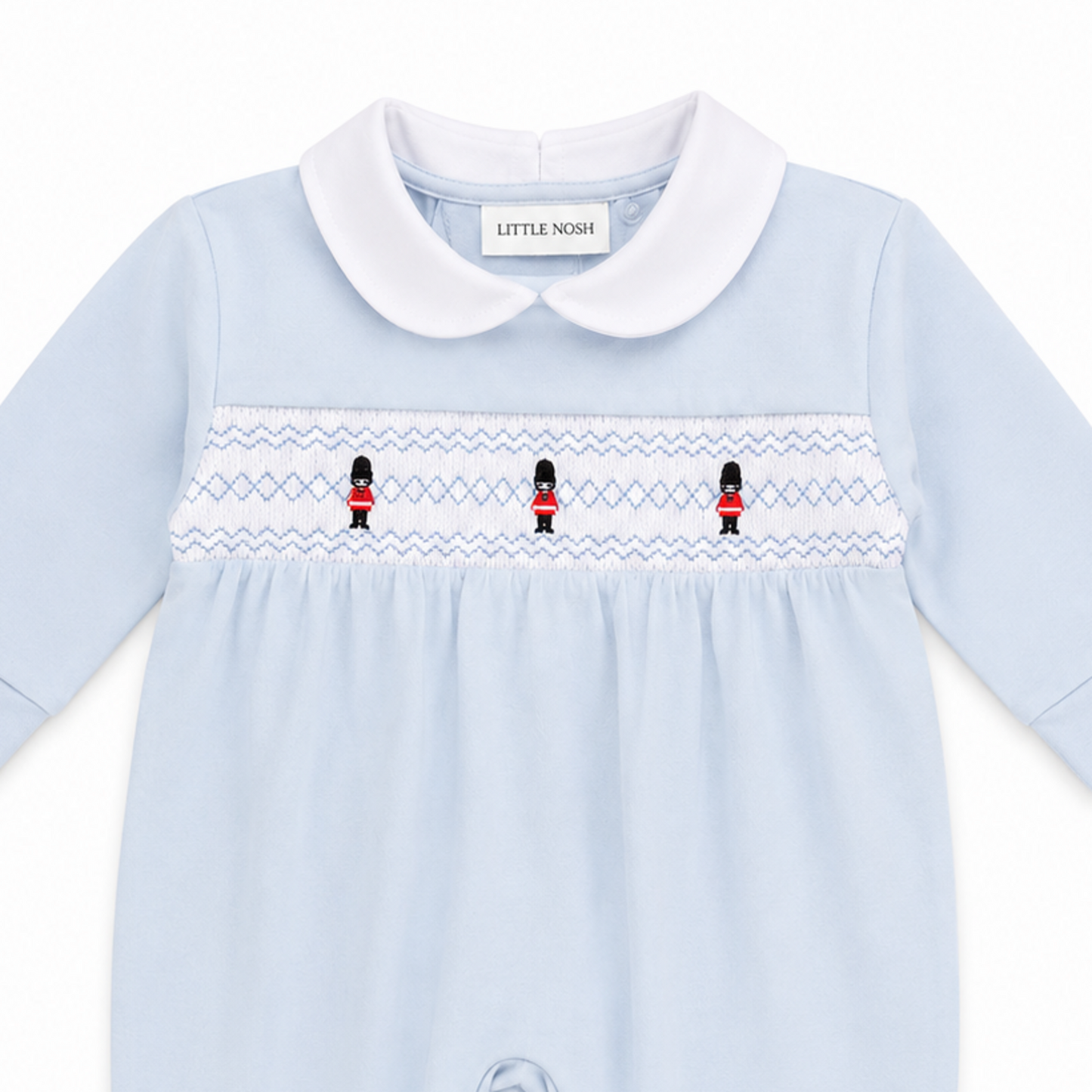Smocked soldier embroidery detail on Little Nosh baby boys blue velour sleepsuit