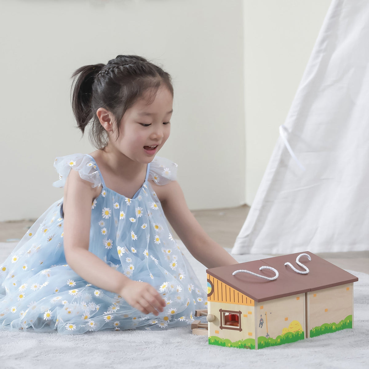 Happy toddler enjoying creative pretend play with a portable wooden farm barn toy.
